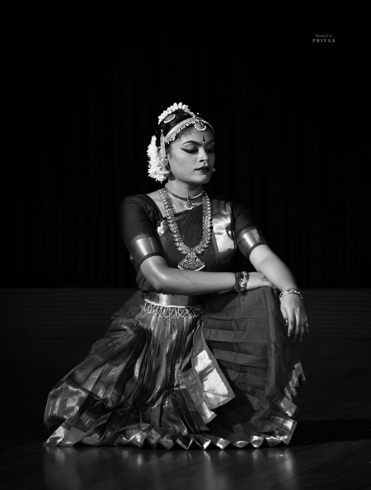 Bharatanatyam dancer seated in a traditional pose, black and white