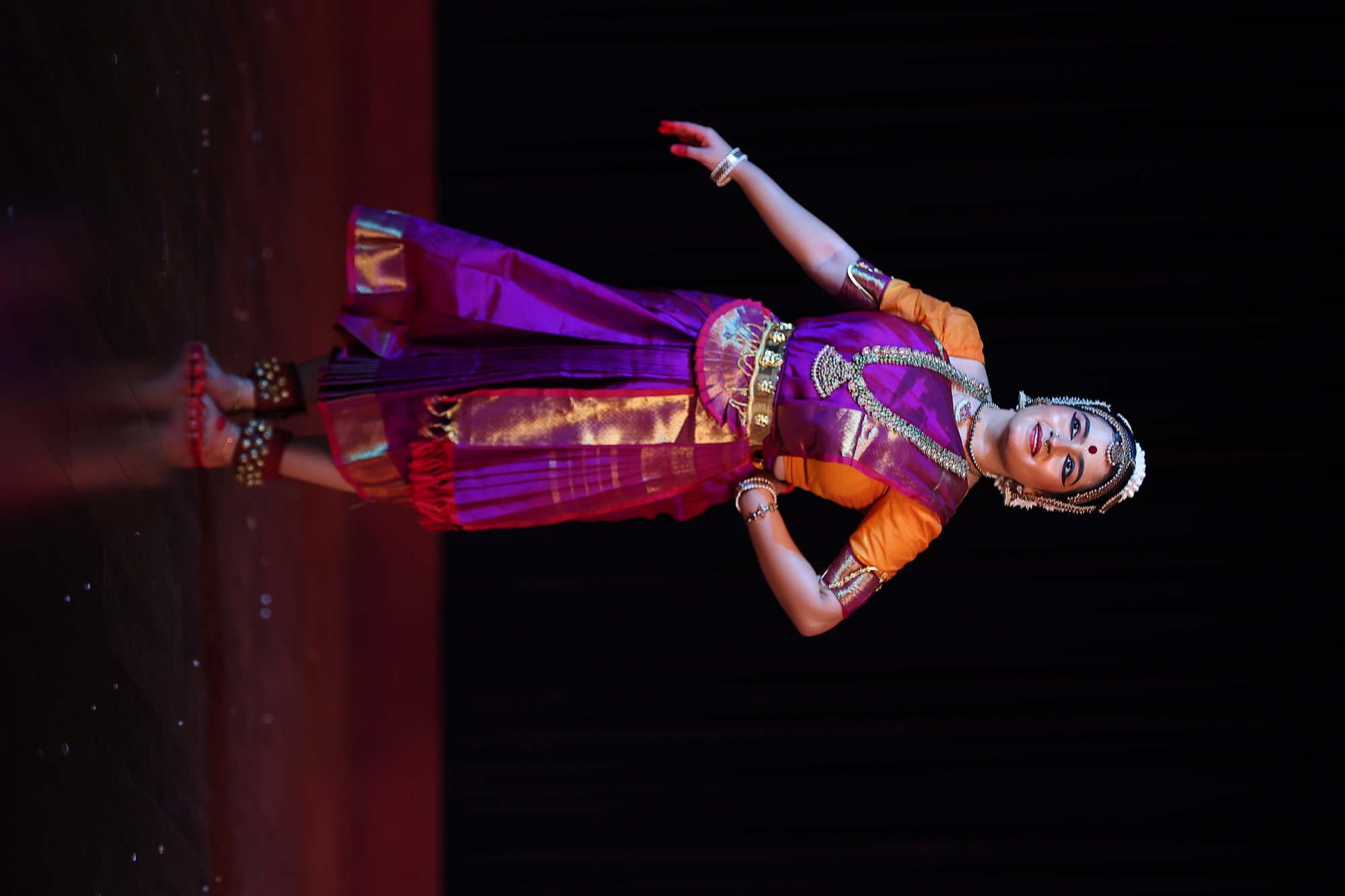 Bharatanatyam dancer in a purple and gold costume, hand on hip