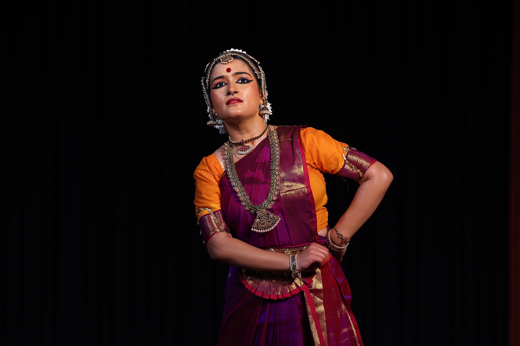 Bharatanatyam dancer in three-quarter profile under warm stage light
